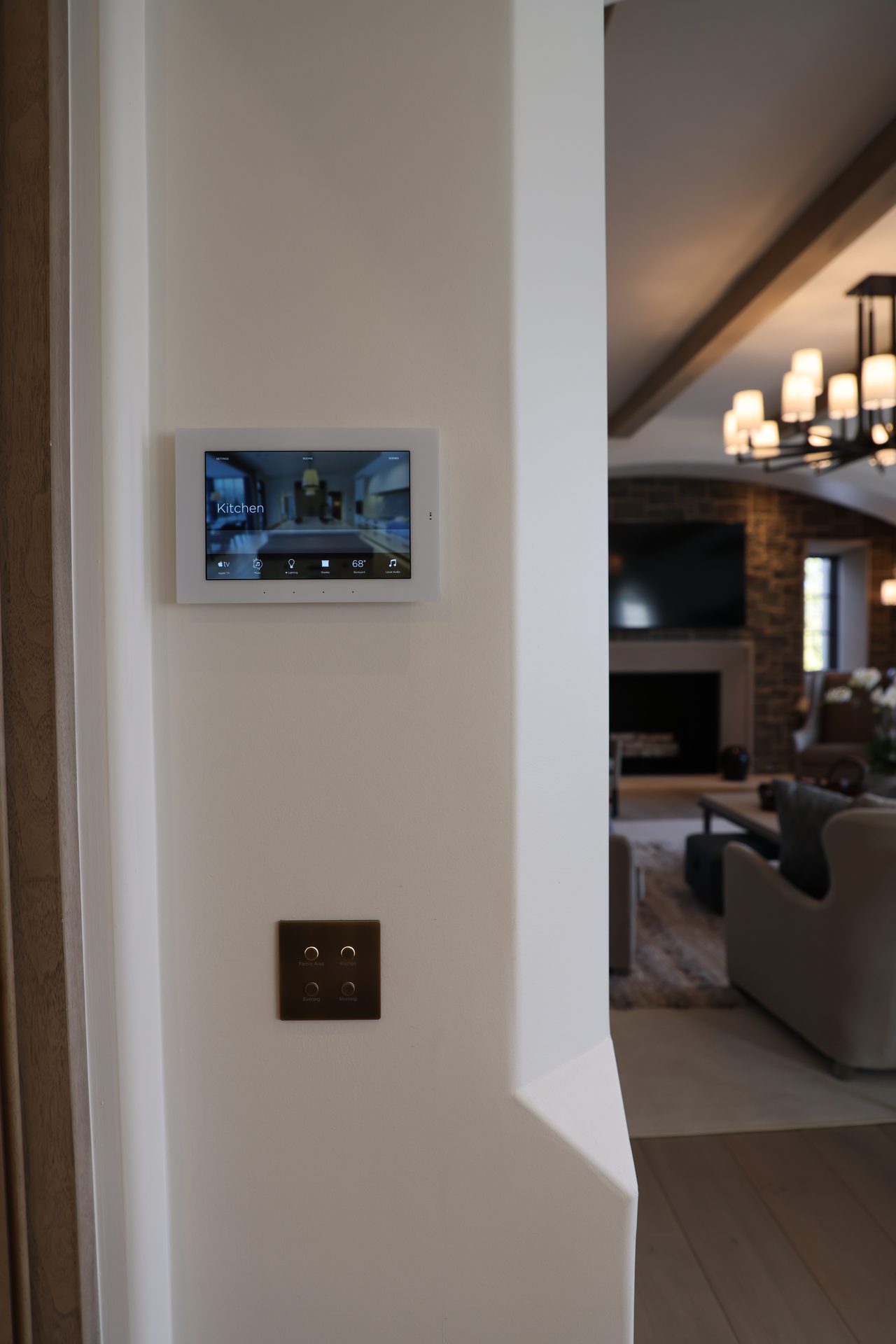 A homeowner tapping a single scene on a tablet or in-wall panel in a bright kitchen; the room visibly responding.